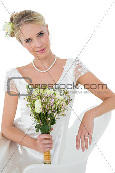 Bride holding flower bouquet while sitting on chair