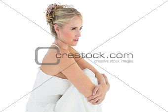 Thoughtful bride hugging knees over white background