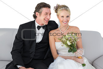 Happy bride sitting with groom on sofa over white background