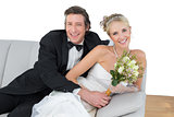 Bride and groom with flower bouquet sitting on sofa