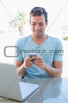 Man text messaging while using laptop