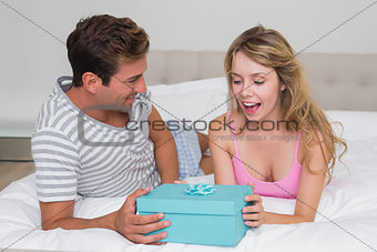 Man giving surprised woman gift box in bed