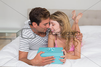 Smiling young couple with gift box in bed