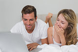 Young couple using laptop in bed at home