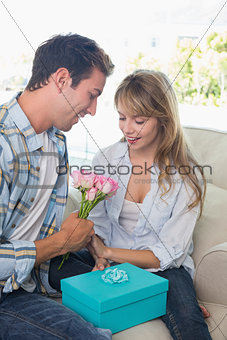Couple with flowers and gift box sitting on sofa