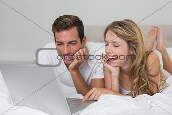 Happy young couple using laptop in bed