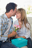 Young man kissing woman with flowers and gift box