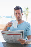 Concentrated man drinking coffee and reading newspaper