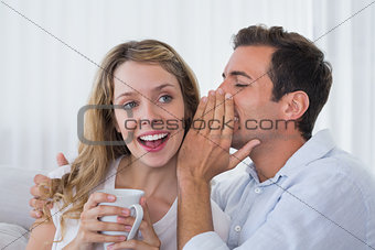 Man whispering secret into a cheerful young womans ear