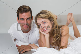 Smiling young couple using laptop in bed