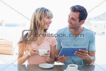 Happy couple using digital tablet while having coffee