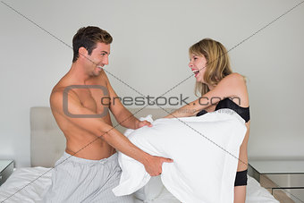 Cheerful semi nude couple pillow fighting in bed