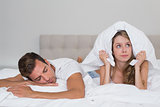 Angry woman holding pillow besides sleeping man in bed