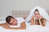 Angry woman holding pillow besides a sleeping man in bed