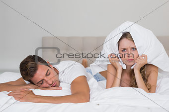 Angry woman holding pillow besides a sleeping man in bed