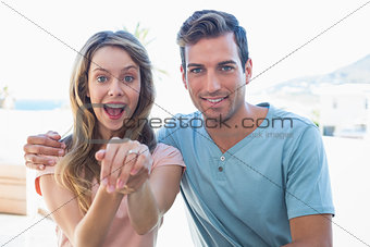 Cheerful woman showing engagement ring besides man
