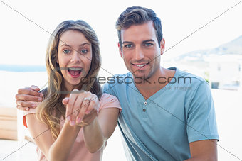 Cheerful woman showing engagement ring besides man
