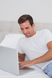 Smiling relaxed man using laptop in bed