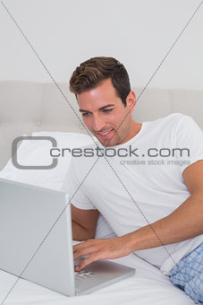 Smiling relaxed man using laptop in bed