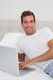 Smiling young man using laptop in bed