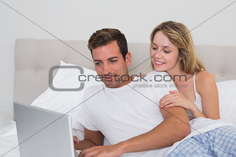 Relaxed smiling couple using laptop in bed