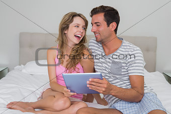Cheerful couple using digital tablet in bed