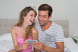 Cheerful couple reading text message in bed
