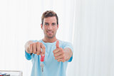 Man holding out new house key while gesturing thumbs up