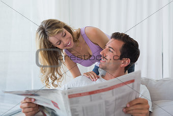 Couple looking at each other while reading newspaper