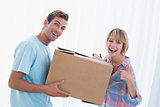 Happy couple carrying cardboard box in new house