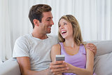 Cheerful couple text messaging on couch