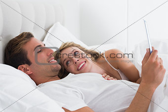 Relaxed couple using digital tablet in bed