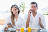 Couple using mobile phones while having breakfast