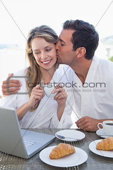 Man kissing woman while using laptop on breakfast table