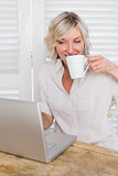 Mature woman drinking coffee while using laptop