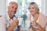 Smiling mature couple with coffee cups at home
