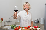 Happy mature woman with vegetables and wine glass in kitchen