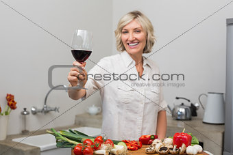 Happy mature woman with vegetables and wine glass in kitchen