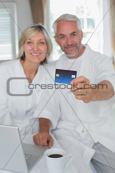 Happy mature couple holding out credit card at home