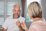 Happy mature man playing cards with woman at home