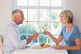Side view of a mature couple toasting drinks over food