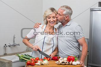 Man kissing woman as she chops vegetables in kitchen