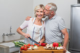 Man kissing woman as she chops vegetables in kitchen