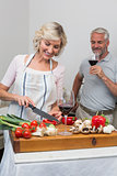 Man with wine glass and woman chopping vegetables in kitchen