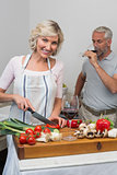 Mature man with wine glass and woman chopping vegetables in kitchen