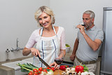 Mature man with wine glass and woman chopping vegetables in kitchen