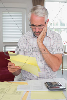 Serious man sitting with home bills and calculator