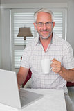 Mature man using laptop while drinking coffee