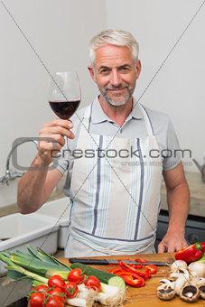 Mature man with wine glass while chopping vegetables in kitchen