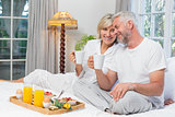 Smiling mature couple with coffee cups sitting on bed